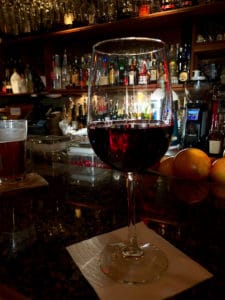 A glass of robust red wine sits on a wooden bar area. 