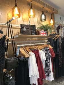 Women's shirts and tank tops in white, black, and red are displayed below large light fitures. 