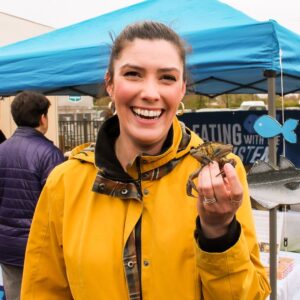 Woman in yellow raincoat holding up green crab