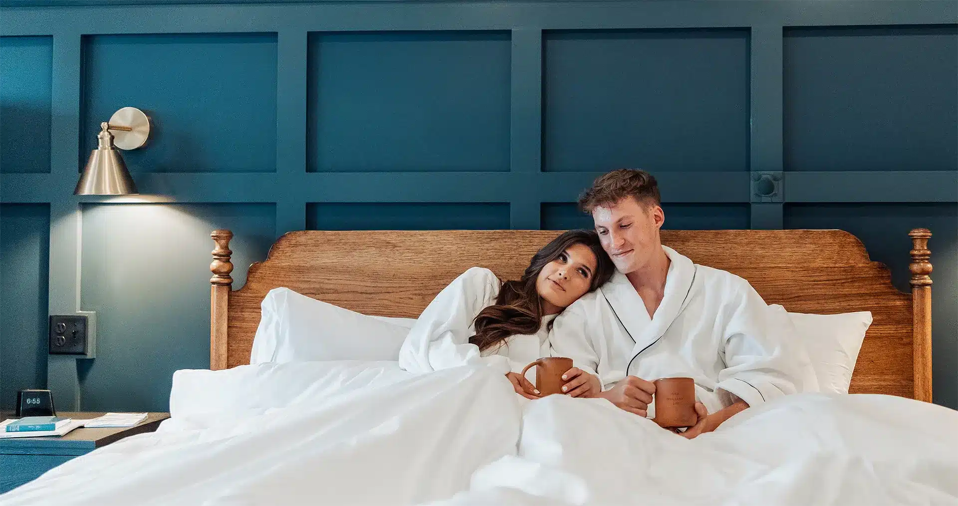 Couple relaxing in bed together while wearing robes and drinking coffee